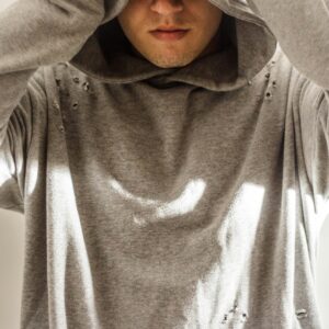 Close-up of a man in a gray hoodie, face partially obscured, soft light indoors.